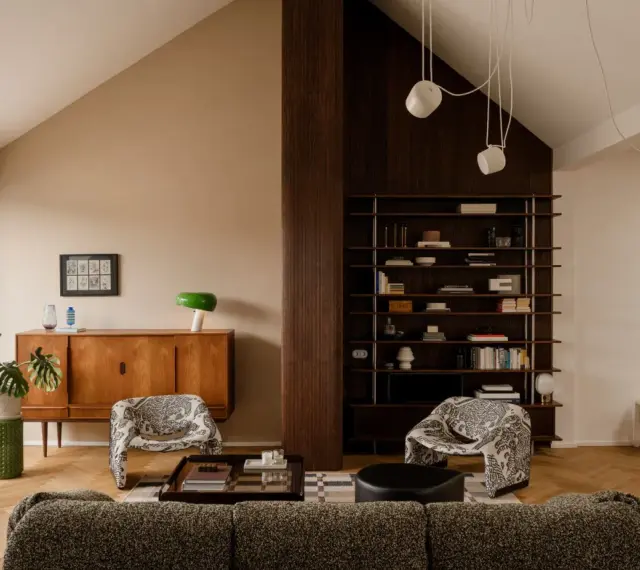 Salón acogedor con **techo inclinado interior**, muebles de madera, estanterías y sillones estampados.