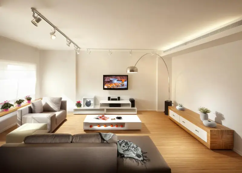 Iluminar un salón moderno con luces de riel y lámpara de arco. Sofás grises, mesa de centro blanca y mueble de TV.