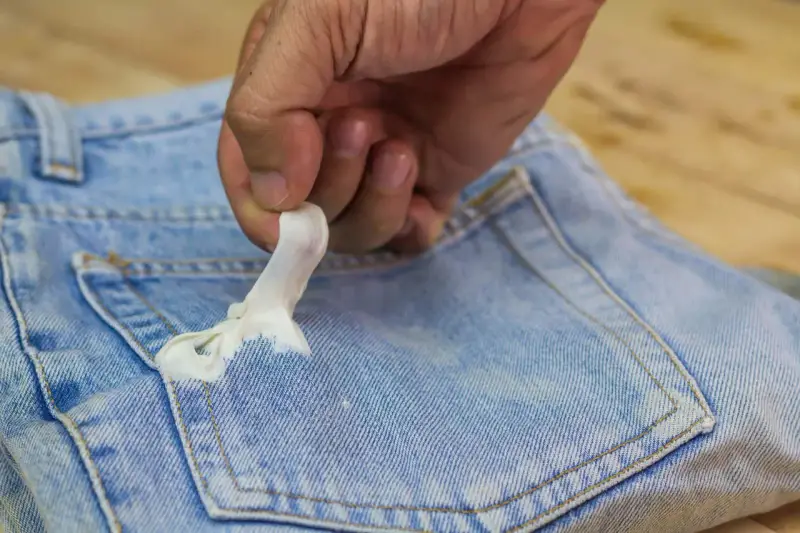 Mano quitando chicle pegado en bolsillo de jeans. Aprende como quitar chicle de la ropa fácilmente.